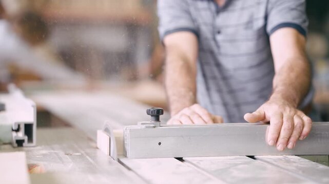 Skilled male worker cutting wood plank with a circular saw in a carpentry workshop. Close up of professional craftsman hands working