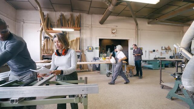 Busy carpentry workshop with skilled artisans collaborating on various projects. Male carpenter using a table saw while colleagues work in the background