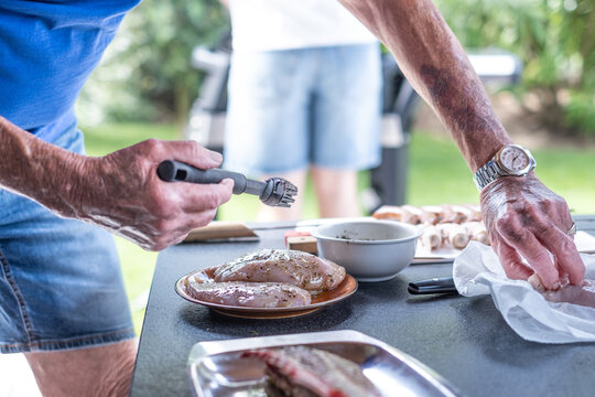Man preparing chicken breasts for an outdoor barbecue party, using a meat tenderizer and seasoning fresh poultry for grilling in the garden
