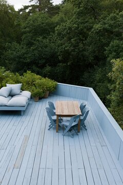 Spacious painted deck with wooden dining table and lounge daybed for outdoor entertaining and peaceful rooftop patio background design