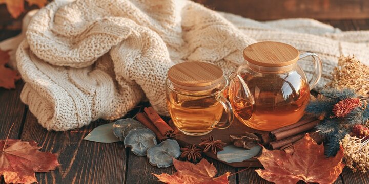 Cozy fall tea set with glass teapot and small mug on wooden board with knit blanket and autumn leaves for harvest wallpaper and poster design