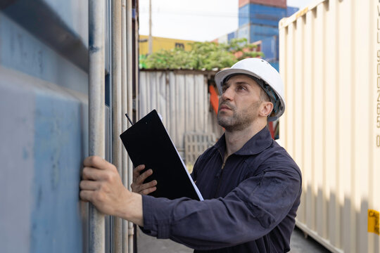Male worker at container yard, with clipboard checklist shipping container transporting imports, exports of goods. Male worker inspect transportation shipping container at container yard