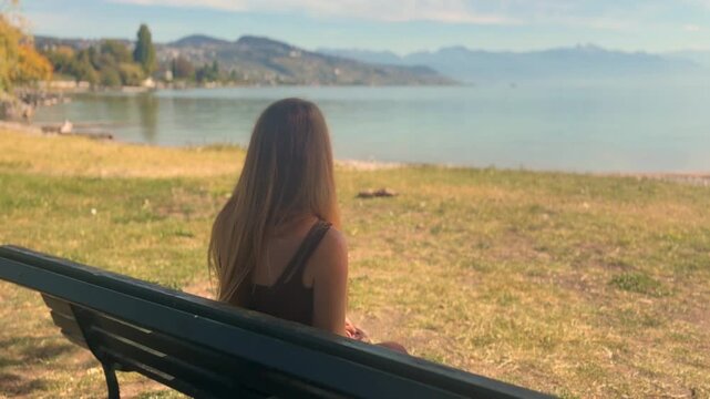 Blonde Woman Sitting on Park Bench Looking at Lake Geneva in Switzerland