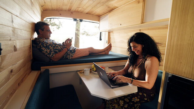 Couple working remotely and relaxing inside a modern wooden camper van, living the freedom of travel and remote work