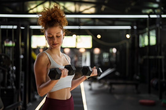 Young woman lifting dumbbells performing bicep curls in gym