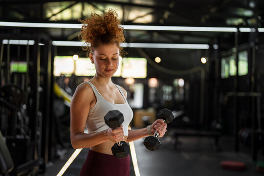 Woman exercising with dumbbells strengthening arm muscles in gym