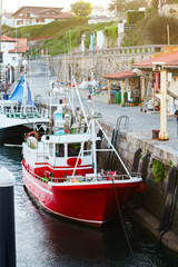 Fototapeta premium A red and white fishing boat docked along a stone pier in a coastal harbor.