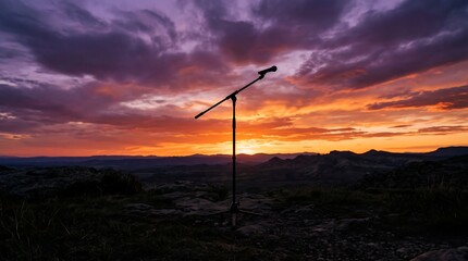 Obraz premium Silhouetted boom microphone stand centered against a vibrant sunset sky with hues of purple orange and yellow over a vast darkened landscape.