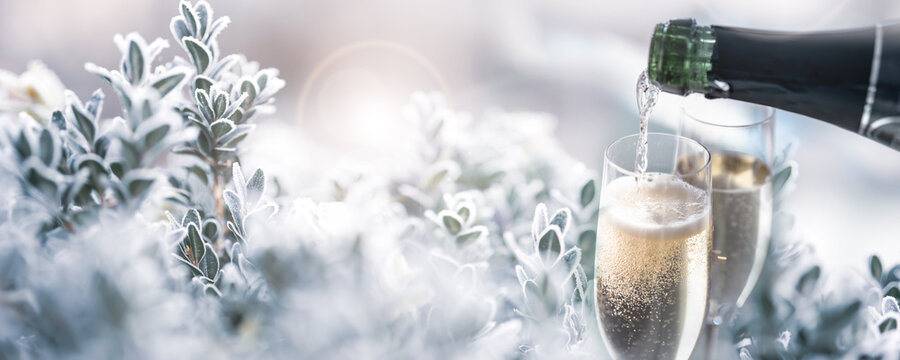 Two glasses of champagne with frozen branches in a snowy winter landscape. Horizontal background with fetsive bokeh for christmas and new year greetings.