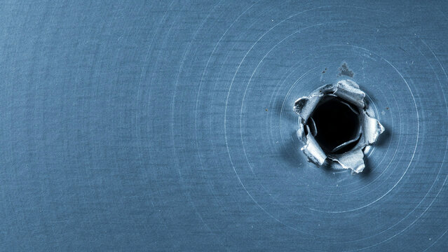 Single bullet hole in a blue metal surface with visible impact damage and circular stress marks