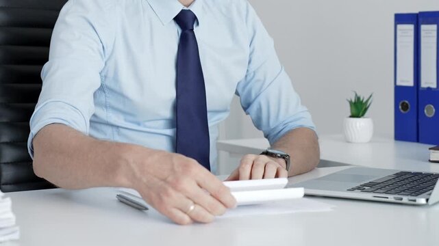 Mature businessman working on a laptop computer at his office desk, typing and focusing on business tasks with document binders and paperwork visible in the background