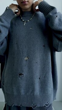 Young man in grey distressed knit sweater with holes and cross necklace closeup