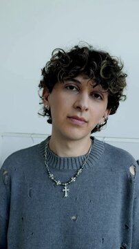 Portrait of young man with curly hair in grey knit sweater with cross necklace