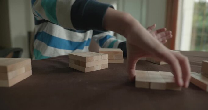Close-up children's hands play with wooden bricks constructing structures. 4K 10-bit