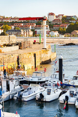 Fototapeta premium Small fishing boats and motorboats docked along a floating pontoon inside a stone harbor basin.