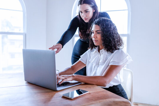 Two women, one Black and one white, collaborating on a laptop in an office