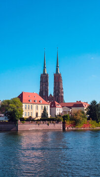Riverside view of twin spired historic cathedral and colorful buildings beside calm water under a clear blue sky in Wroclaw Poland cityscape