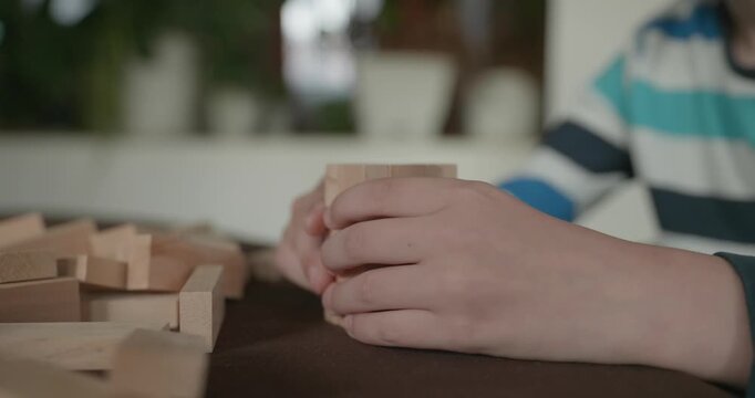 Close-up children's hands play with wooden bricks constructing structures. 4K 10-bit