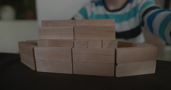 Close-up children's hands play with wooden bricks constructing structures. 4K 10-bit
