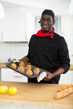 Proffesional man in black chef uniform holding sheet pan with just baked cupcakes