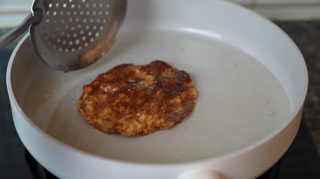  Close up footage of a slotted spoon lifting a fried melinjo cracker from hot oil. This is part of preparing emping manis, a traditional Indonesian sweet snack.
