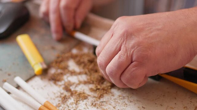Close up of a person using a manual cigarette rolling machine to fill an empty paper tube with tobacco