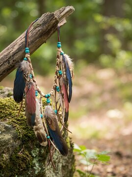 Tribal feather necklace hanging on a wooden branch. Native style handmade jewelry with beads outdoors