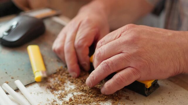 Close up of a person using a manual cigarette rolling machine to fill an empty paper tube with tobacco
