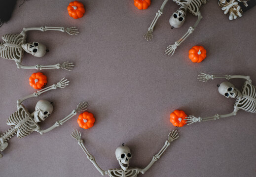Halloween skeletons and pumpkin ornaments flat lay circle frame on grey background