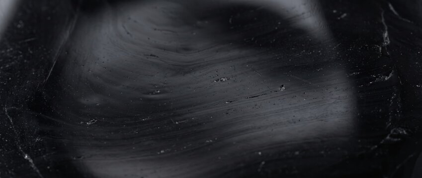 Close-up of thick black viscous liquid with swirling patterns, glossy surface and light