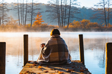 Fototapeta premium Person on a lake dock wrapped in a blanket