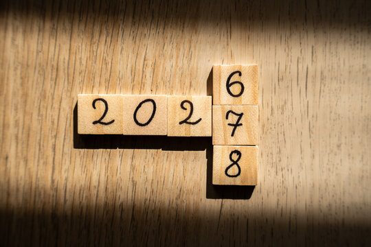 Wooden blocks spelling 202 with a vertical column of 6, 7 and 8, showing years 2026, 2027 and 2028 on an oak desk in a sunbeam, concept of a three year plan, business roadmap and future growth