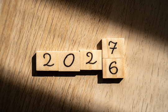 Flat lay of 202 wooden tiles with a 7 placed above the 6, 2026 and 2027 combined in one layout in diagonal sunlight on oak, concept of the year turning over, update and new year resolutions