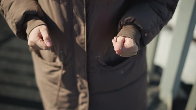 Person wearing thick padded jacket adjusts their sleeve cuffs to keep warm. focus remains on hands and lower torso in outdoor setting with soft natural light emphasizing practical movement