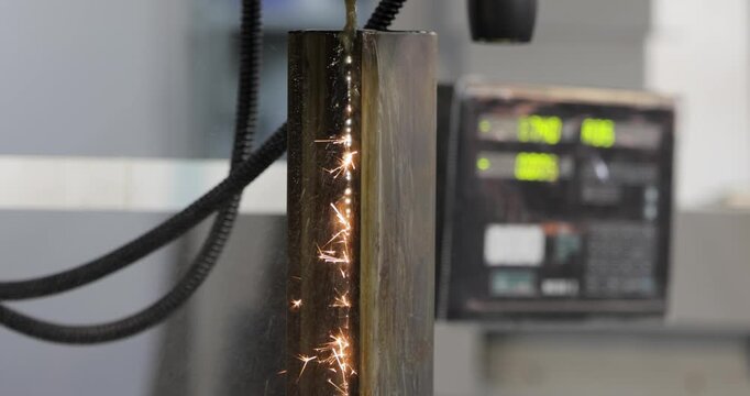 Wire EDM cutting of metal workpiece with sparks in industrial machine.