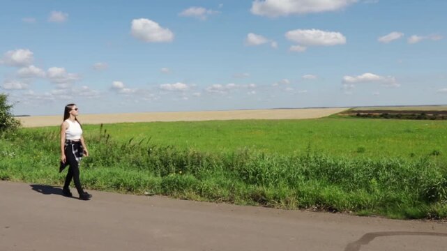 young woman walks past expansive green and golden fields while looking across the rural landscape, illustrating slow travel, mindful movement, summer leisure and outdoor wellbeing