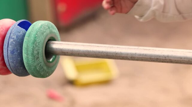 Child hand slides colorful rings along a playground abacus toy bar