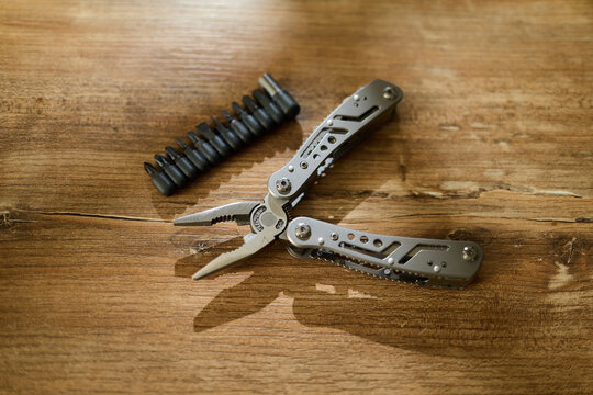 Tool with pliers and interchangeable bits placed on a wooden surface in a workshop setting