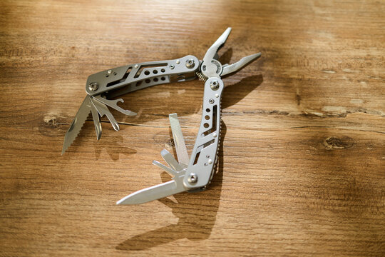 Metal multi-tool with various blades on a wooden surface