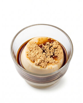 Top-down view of Japanese milk pudding topped with sweet black sugar syrup (kuromitsu) and roasted soybean flour (kinako) in a clear glass bowl, isolated on a white background.