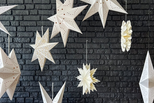 White paper star decorations hanging in front of a dark brick wall background for holiday interior decor