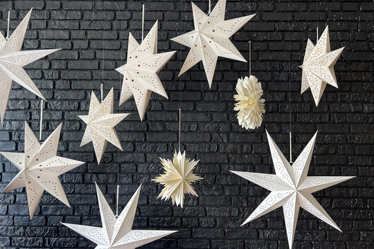 White paper star ornaments hanging in front of a dark brick background