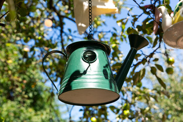 Green metal watering can used as a bird house hanging from a tree branch with a garden background © ir1ska