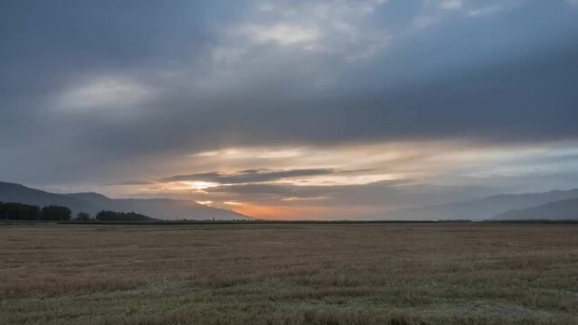 Sunset over harvested wheat field with dramatic cloud cover and mountain range in Xinjiang