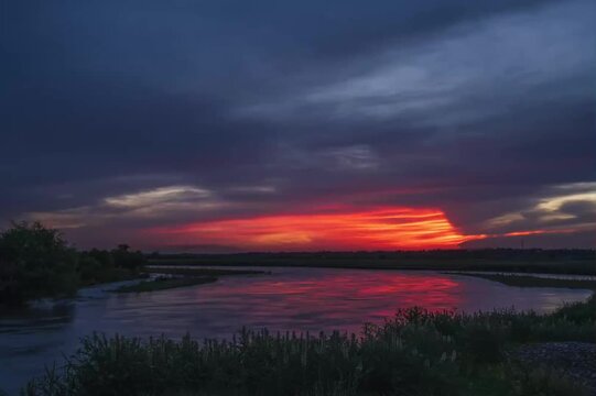 River at sunset with dramatic fiery clouds reflecting on water, Ili River basin landscape