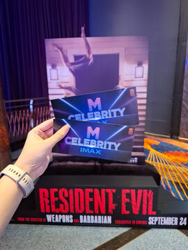 Close up of hand holding two M Celebrity IMAX movie passes in front of Resident Evil promotional cinema display at theater lobby on September 28, 2026 in Bangkok, Thailand 