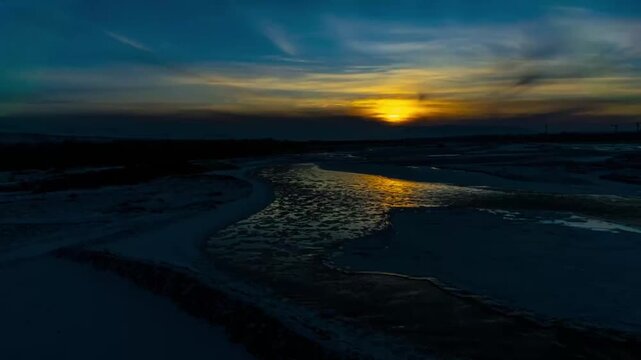 Ili River in Xinjiang at winter sunset, aerial timelapse showing icy riverbed and golden light reflecting on frozen water