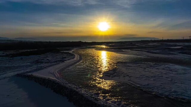 Sunset over the Ili River in Xinjiang with icy banks and golden reflection, aerial drone view
