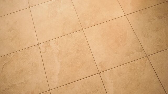 Diagonal view of large beige floor tiles with mottled sandstone texture and thin grout joints, warm amber toned ceramic flooring, natural stone look tile background for interior design, kitchen or ba