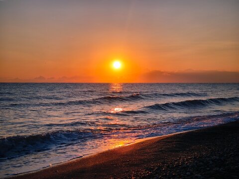 Golden sunset reflection on wet sand beach with calm sea waves bright sun path on ocean water surface scenic orange sky travel background nature.